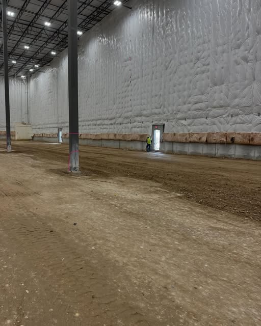 Interior of a large steel commercial building under construction with dirt floor being prepped