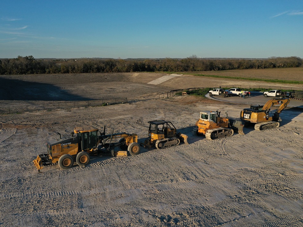 Drone shot of graded pad with grader, dozer, and excavator equipment lineup